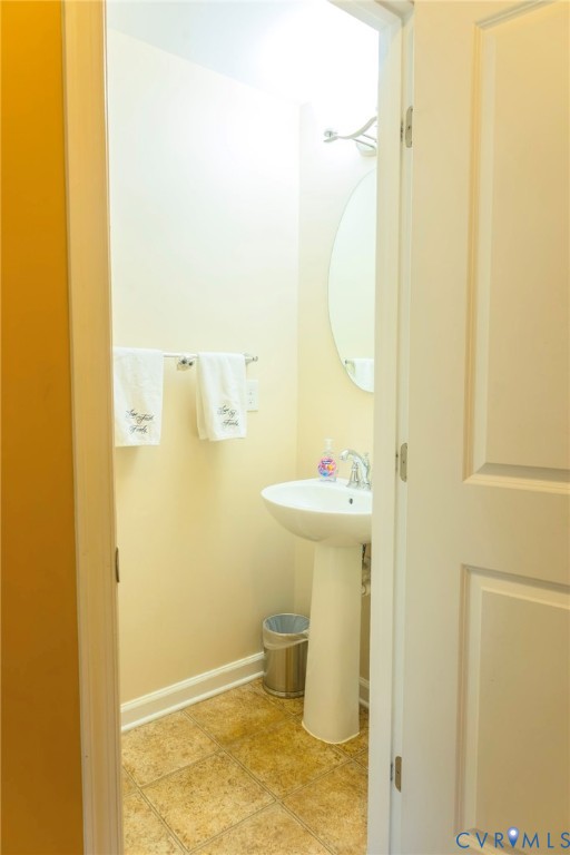 Pedestal sink with chrome faucet, oval wall mirror, and tile flooring