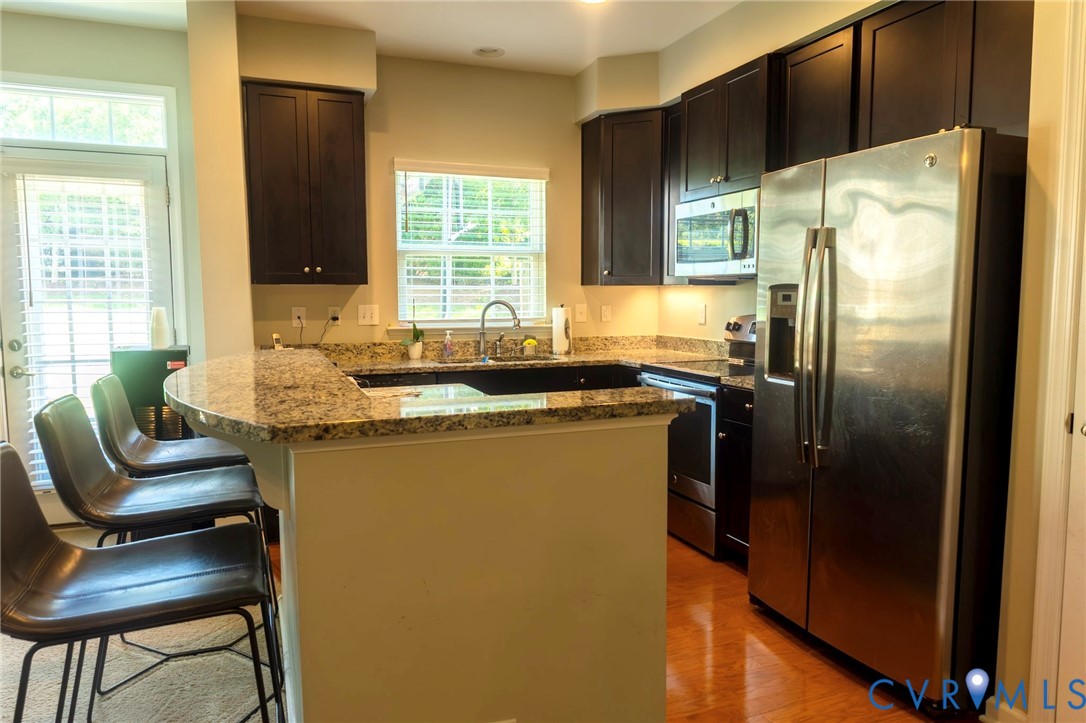 Kitchen featuring dark wood cabinetry, stainless steel appliances, granite countertops, wood-finish flooring, and a breakfast bar