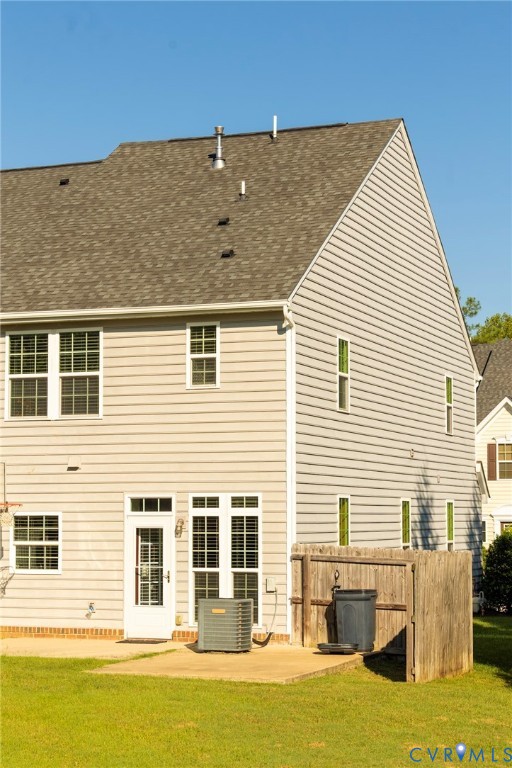 Pitched roof with asphalt shingles, light-toned siding, multiple windows, a rear entry door, and a concrete patio