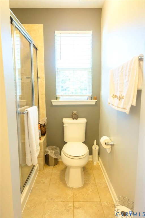 Glass-enclosed shower, neutral tile flooring, white toilet, window with blinds, and towel bar