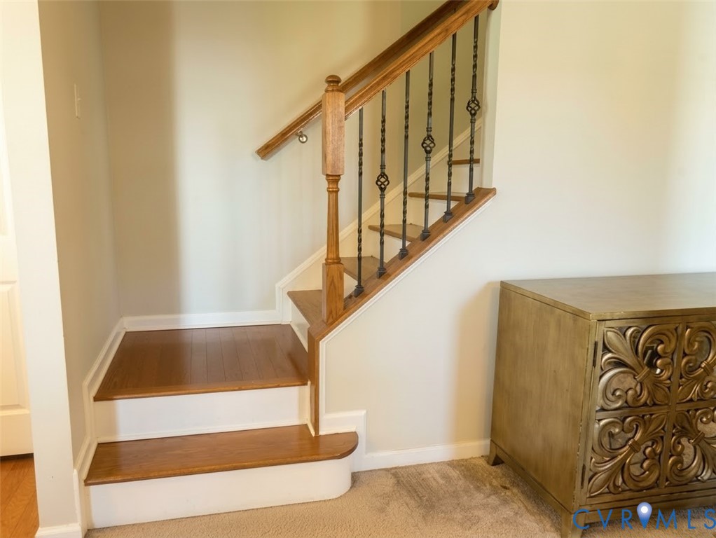 Staircase featuring wood-finish treads, a wood handrail, and decorative iron balusters