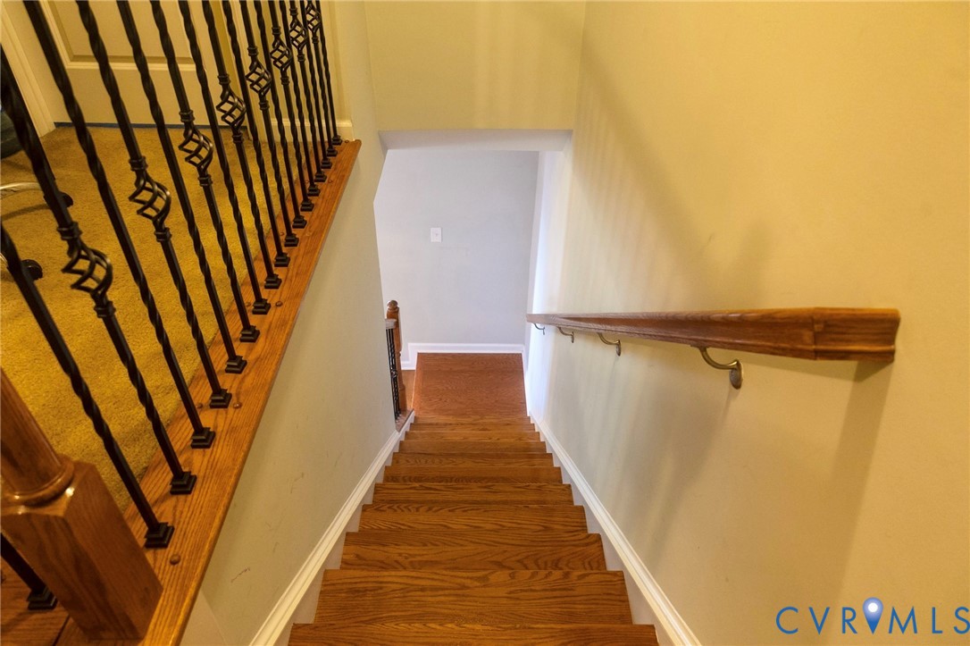 Staircase featuring wood-finish treads, a contrasting wood-finish handrail, and wrought iron balusters with decorative elements