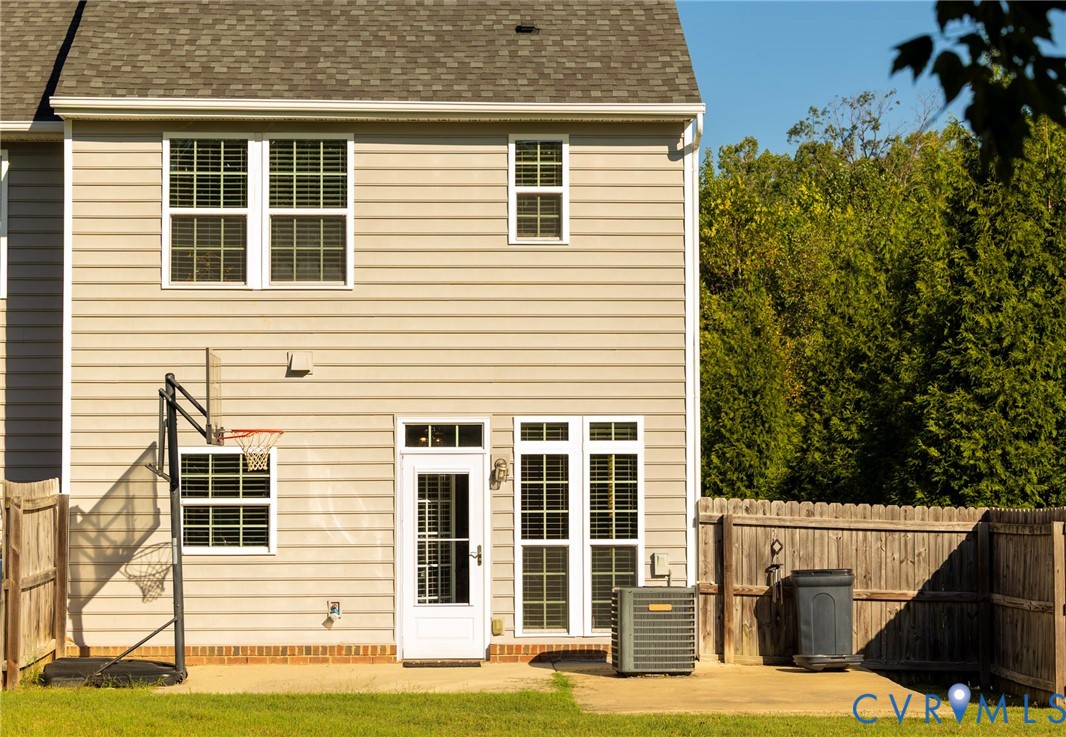 Rear exterior featuring neutral-toned siding, a shingled roof, multiple windows with grilles, and a privacy fence