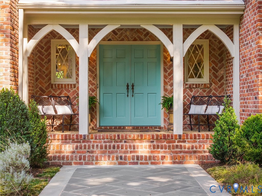 Brick exterior featuring a teal double entry door, an arched portico, diamond-pane windows, and a stone-paver walkway
