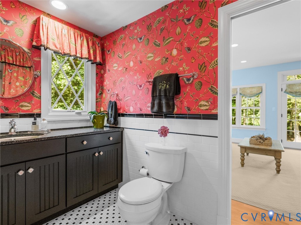 Bathroom featuring an ornate pattern wallpaper, black vanity with an integrated sink, diamond-pattern window, and geometric floor tiling