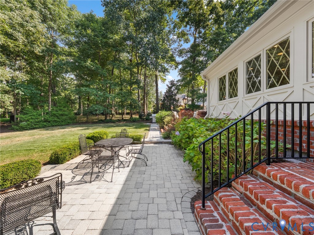 Expansive backyard featuring a manicured lawn, paver patio, brick steps with a black metal railing, and diamond-pane windows