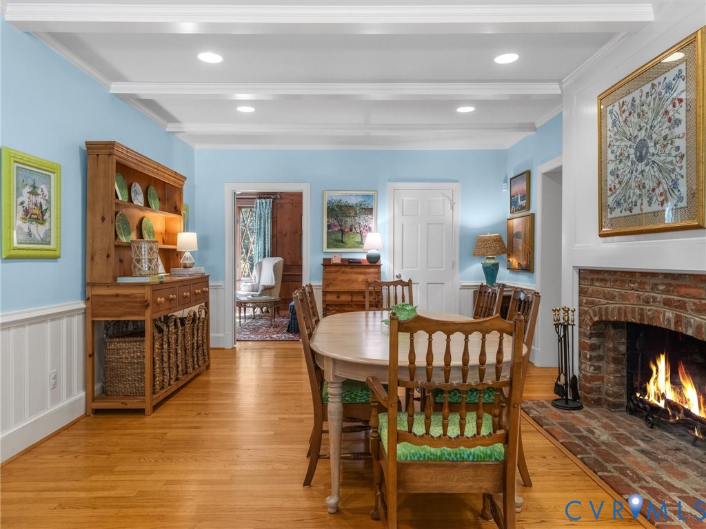 Hardwood flooring, brick fireplace with mantel, white wainscoting, overhead ceiling beams, and recessed lighting