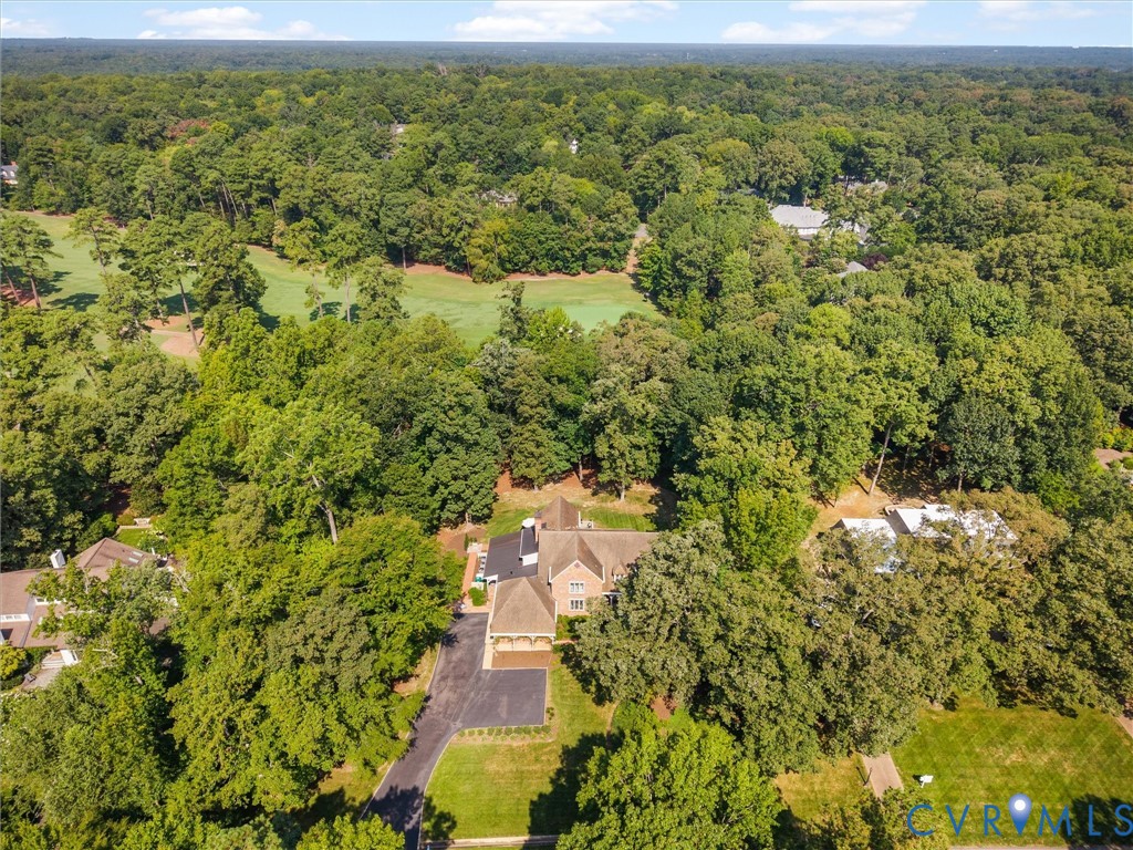 Expansive property surrounded by mature trees, featuring a paved driveway, and a golf course beyond