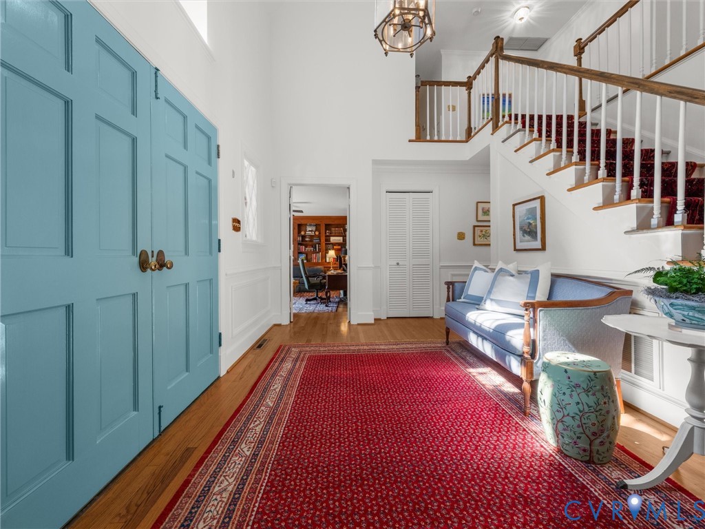 Two-story entry with wood-finish flooring, paneled doors, wainscoting, and a staircase with a wood handrail