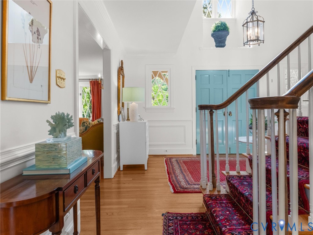 Hardwood flooring, painted blue double doors, white wainscoting, upper transom windows, and a staircase with wood handrail