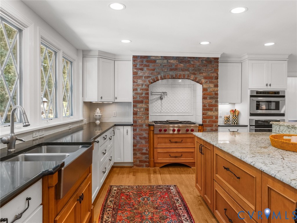 Kitchen featuring white cabinetry, brick archway, stainless steel range, wood-finish flooring, and a center island with a light-toned countertop