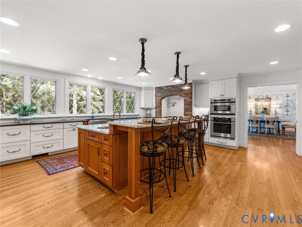 Wood-finish flooring, white cabinetry, granite countertops, built-in stainless steel appliances, and a central island with seating