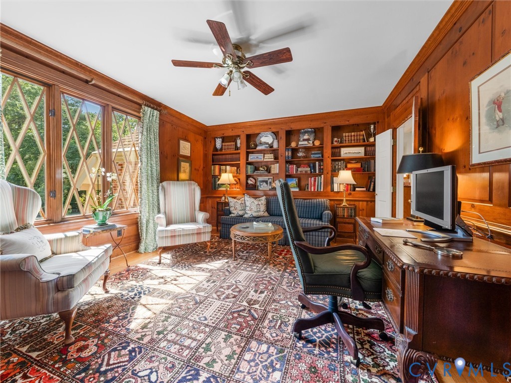 Wood-paneled room featuring built-in shelving, hardwood flooring, and a ceiling fan