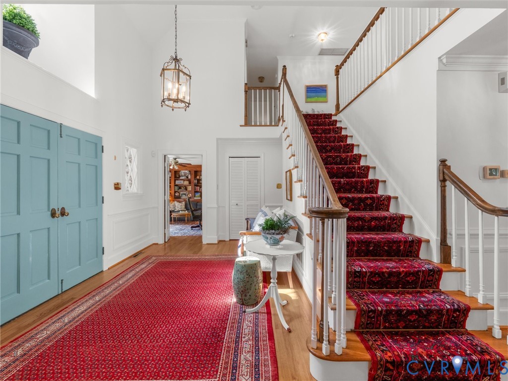 Two-story entryway with hardwood flooring, a prominent staircase with wood handrails, and a chandelier