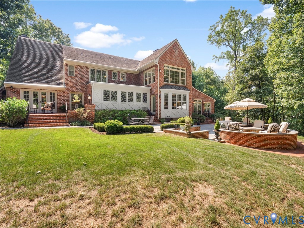 Brick exterior with multiple French doors, an expansive lawn, a patio, and a built-in brick fire pit