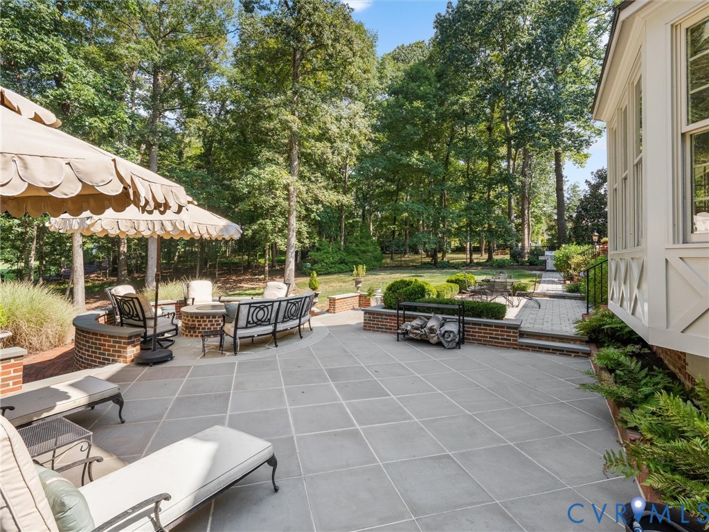 Expansive stone patio featuring a built-in brick fire pit, a curved brick retaining wall, and mature landscaping