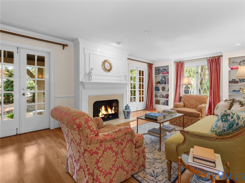 Hardwood flooring, a fireplace with a detailed mantel, built-in shelving, and French doors