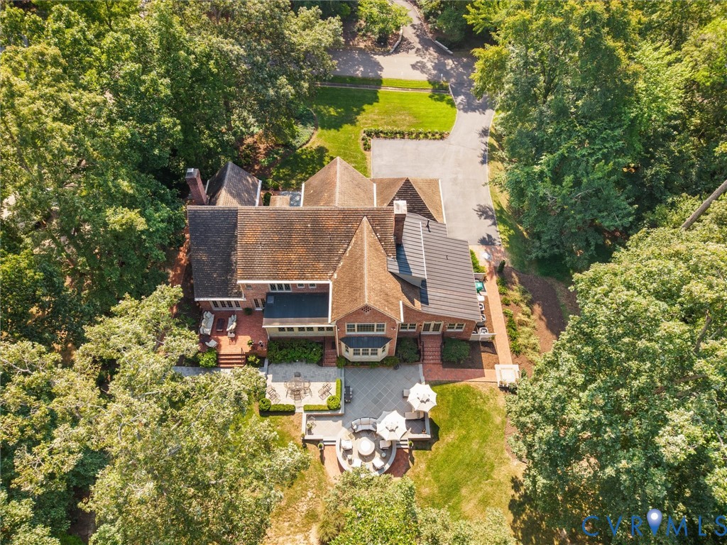Brick exterior with multiple gabled roofs, extensive paved driveway, and multiple outdoor patio areas