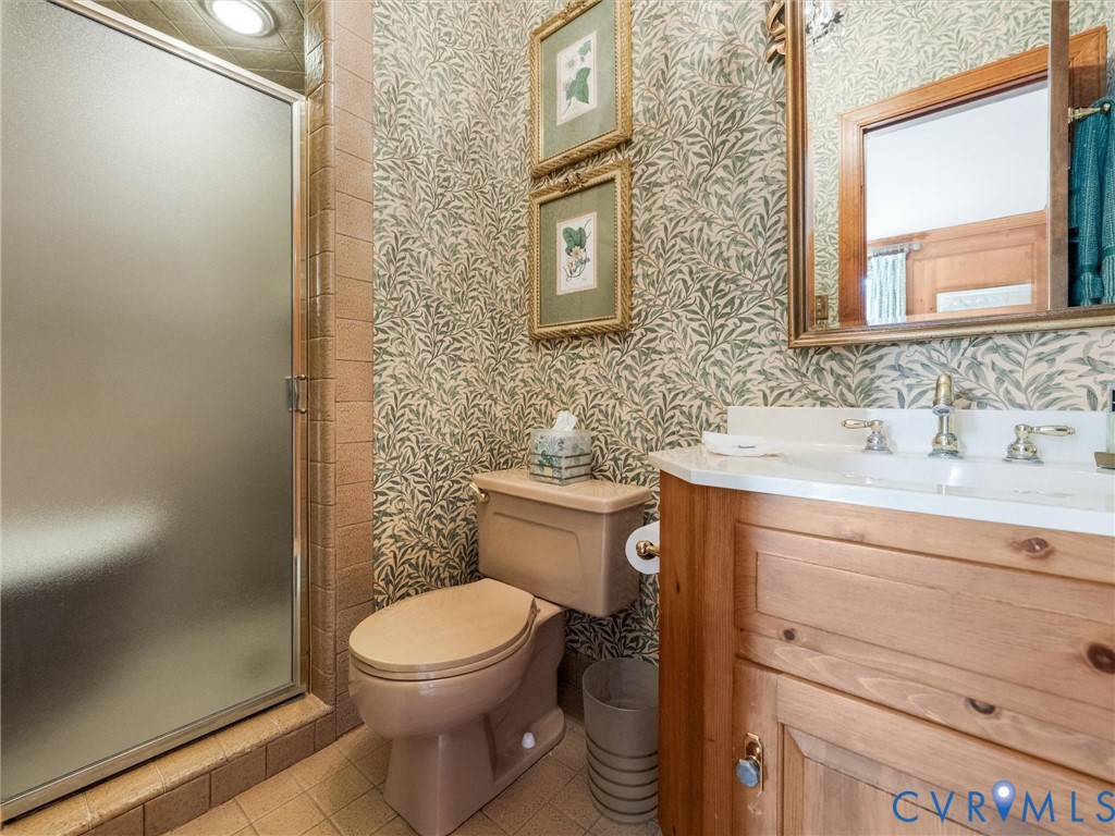 Frosted glass shower enclosure, single vanity with wood-finish cabinetry, white countertop, and dual-handle faucet