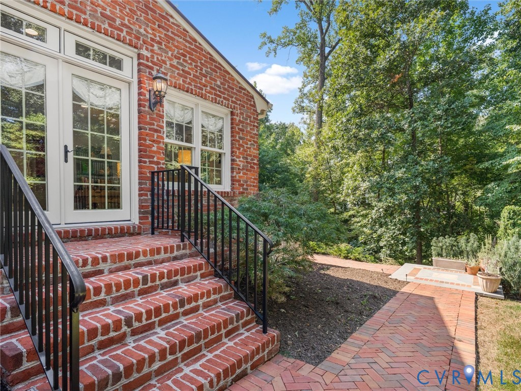 Brick exterior with white-framed double doors, black metal railings, brick steps, and a brick pathway