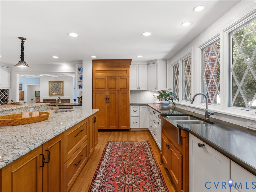 Kitchen featuring wood-finish flooring, an expansive island with granite countertops, abundant cabinetry, a built-in refrigerator, and multiple windows