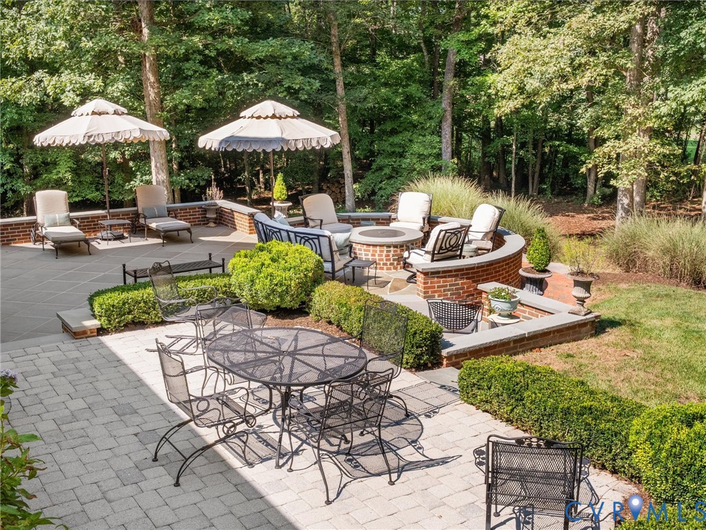 Multi-level paver patio featuring a built-in fire pit with brick surround, low brick walls, and integrated landscaping with manicured hedges