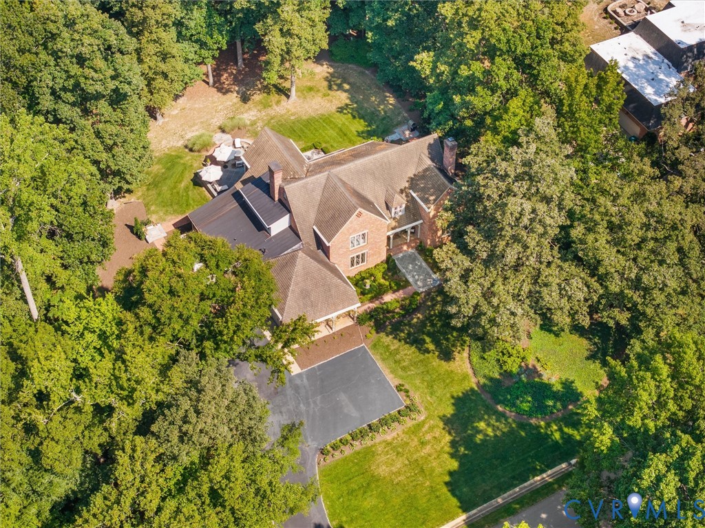 Brick exterior residence featuring a multi-gabled roofline, mature trees, a paved driveway, and a manicured lawn