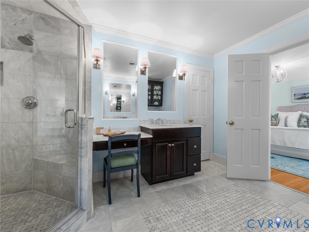 Glass-enclosed shower with a built-in bench, dual vanity with undermount sinks, wall-mounted sconces, and light-toned tile flooring
