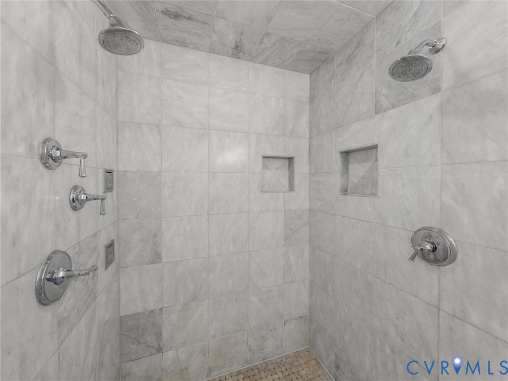 Tiled shower enclosure featuring dual shower heads, multiple control valves, and recessed shelving