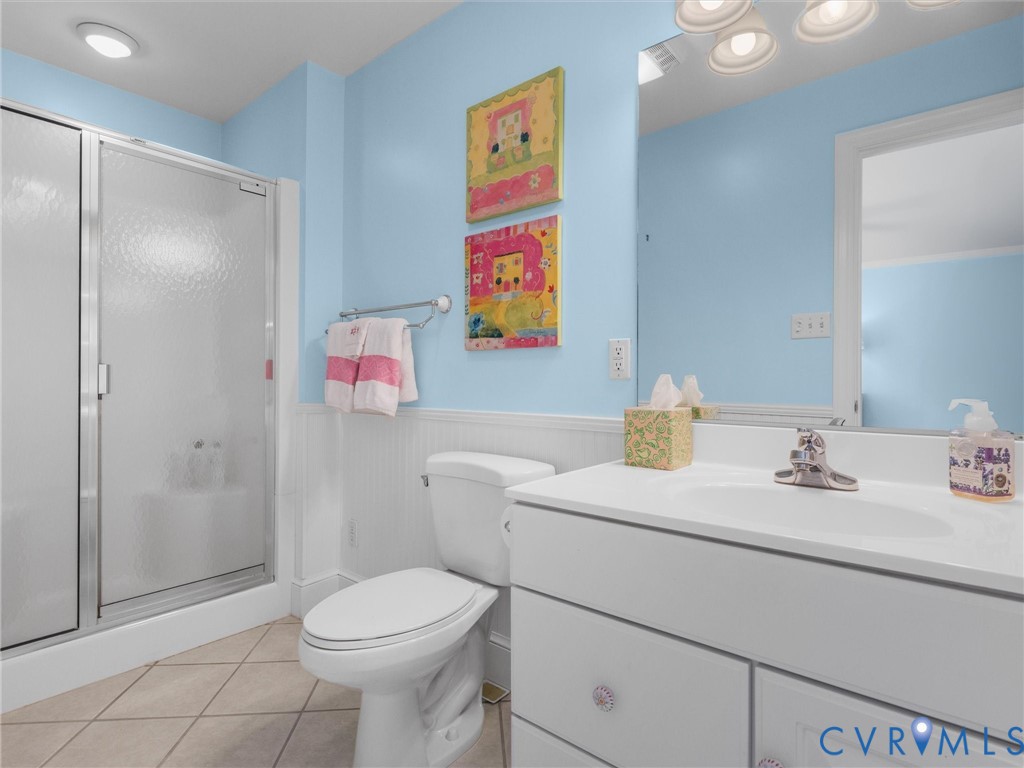 Shower with sliding frosted glass door, white vanity with integrated sink, chrome faucet, white beadboard wainscoting, and tile flooring