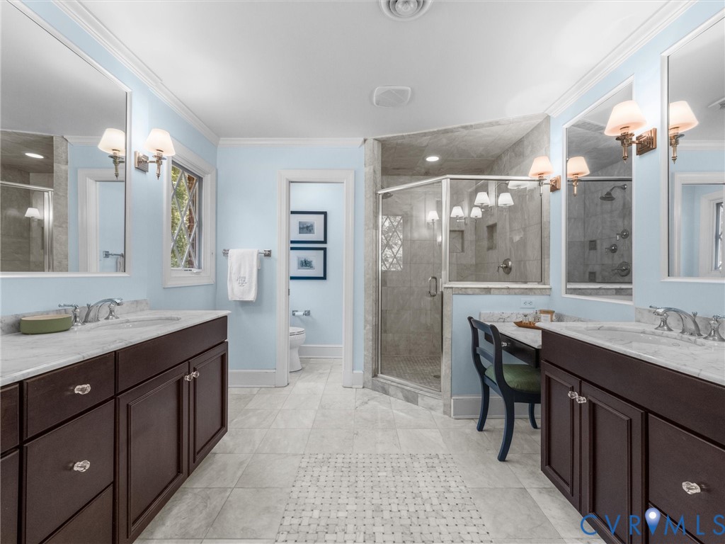 Dual vanity with marble countertops, a separate shower enclosure with a glass door, a built-in vanity station, and a decorative window