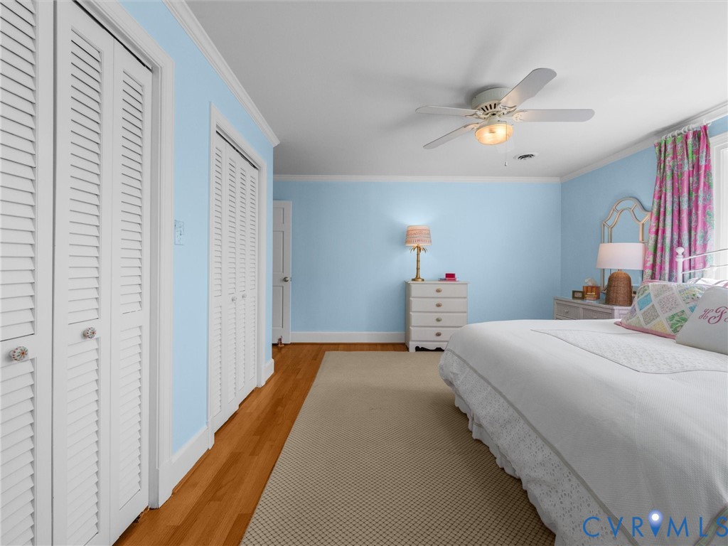 Hardwood flooring, crown molding, white louvered bifold doors, and a ceiling fan with light fixture