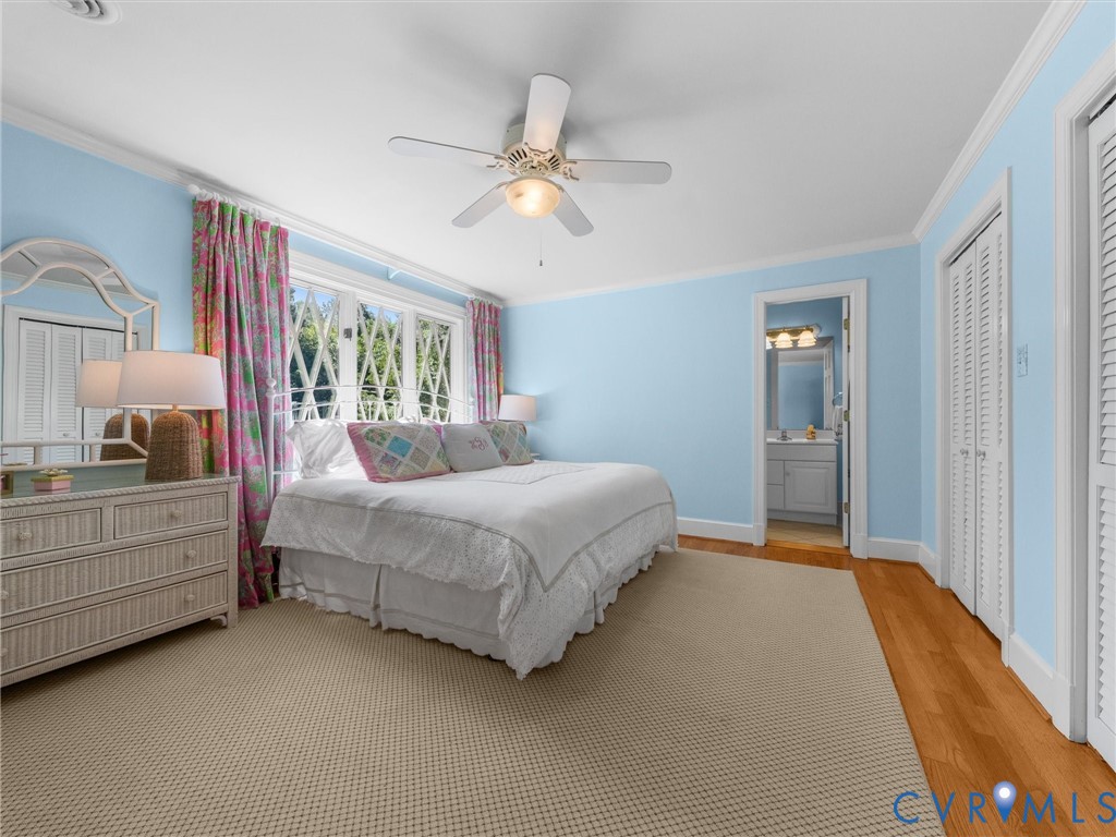 Hardwood flooring, light blue wall paint, ceiling fan, white crown molding, and louvered closet doors