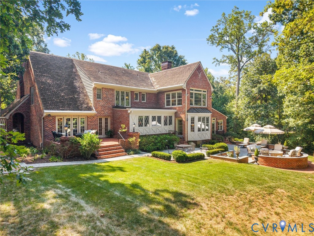 Brick exterior with multiple gabled rooflines, expansive lawn, multi-level brick patio, and mature trees