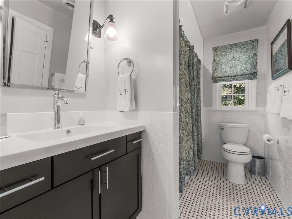 Vanity with a white countertop and dark cabinetry, chrome faucet, wall-mounted mirror, and tile flooring