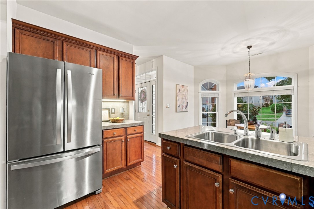 Kitchen featuring wood-finish flooring, wood cabinetry with crown molding, stainless steel refrigerator, and a double basin sink with a chrome faucet