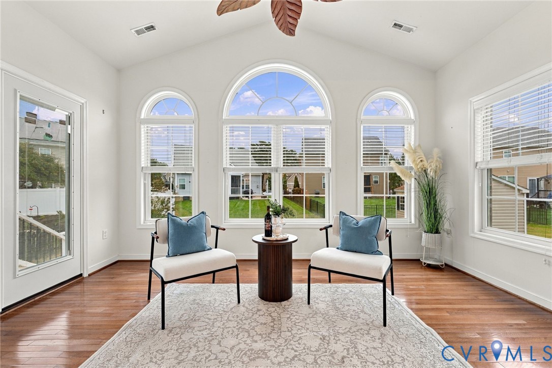 Vaulted ceiling with a ceiling fan, arched windows, rectangular windows with blinds, wood-finish flooring, and a glass-paneled door