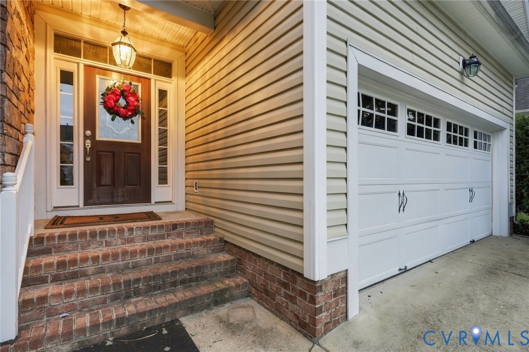 Brick stairs and foundation, wood-panel entry door with sidelights, overhead entry light fixture, and white paneled garage door with window inserts