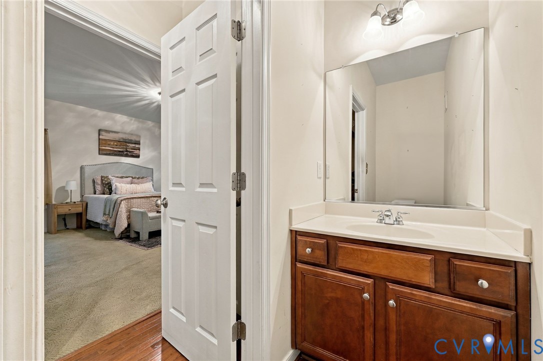 Wood-finish flooring leading into a carpeted room with a built-in vanity, integrated sink, and an overhead light fixture