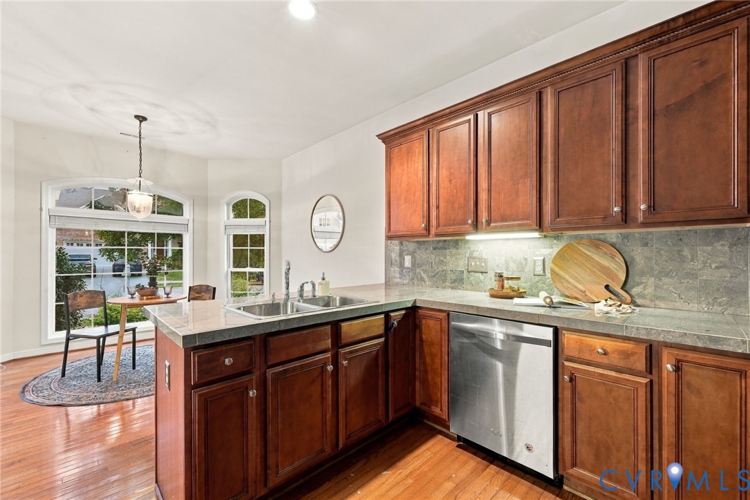 Kitchen featuring wood-finish cabinetry, stainless steel dishwasher, tile backsplash, and light-toned countertops