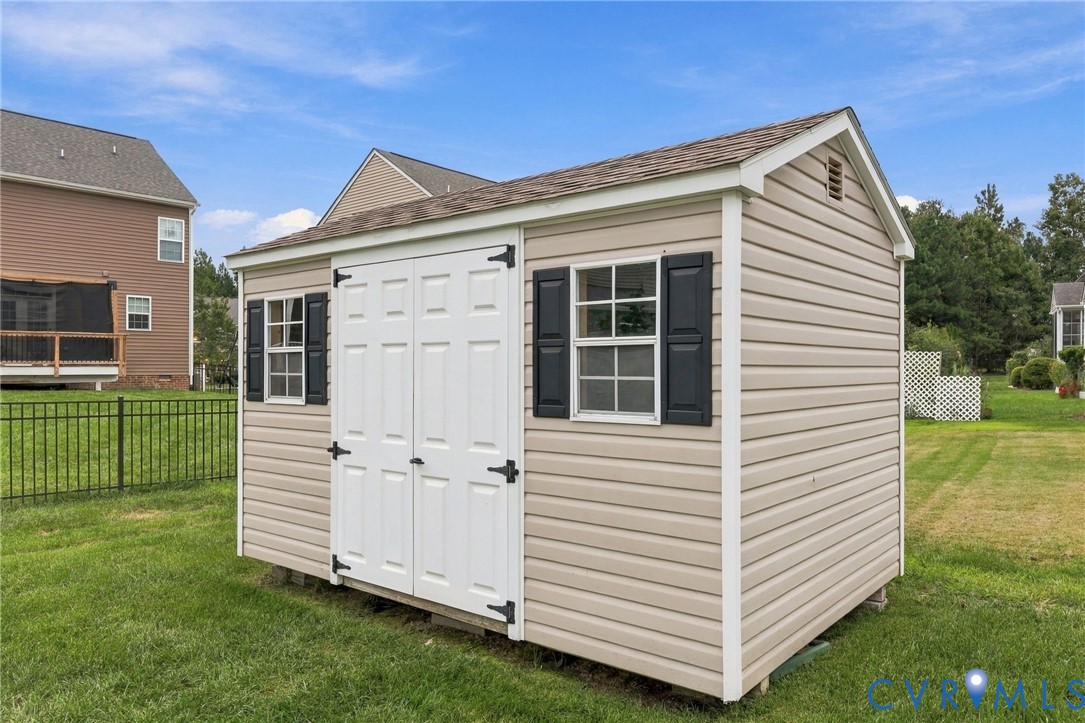 Detached shed with vinyl siding, white double doors, and black window shutters
