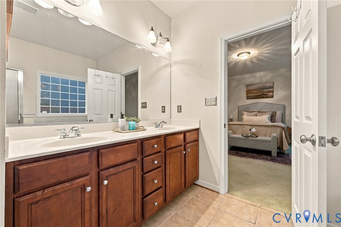 Double vanity with wood cabinetry and undermount sinks, large wall-mounted mirror, and tile flooring