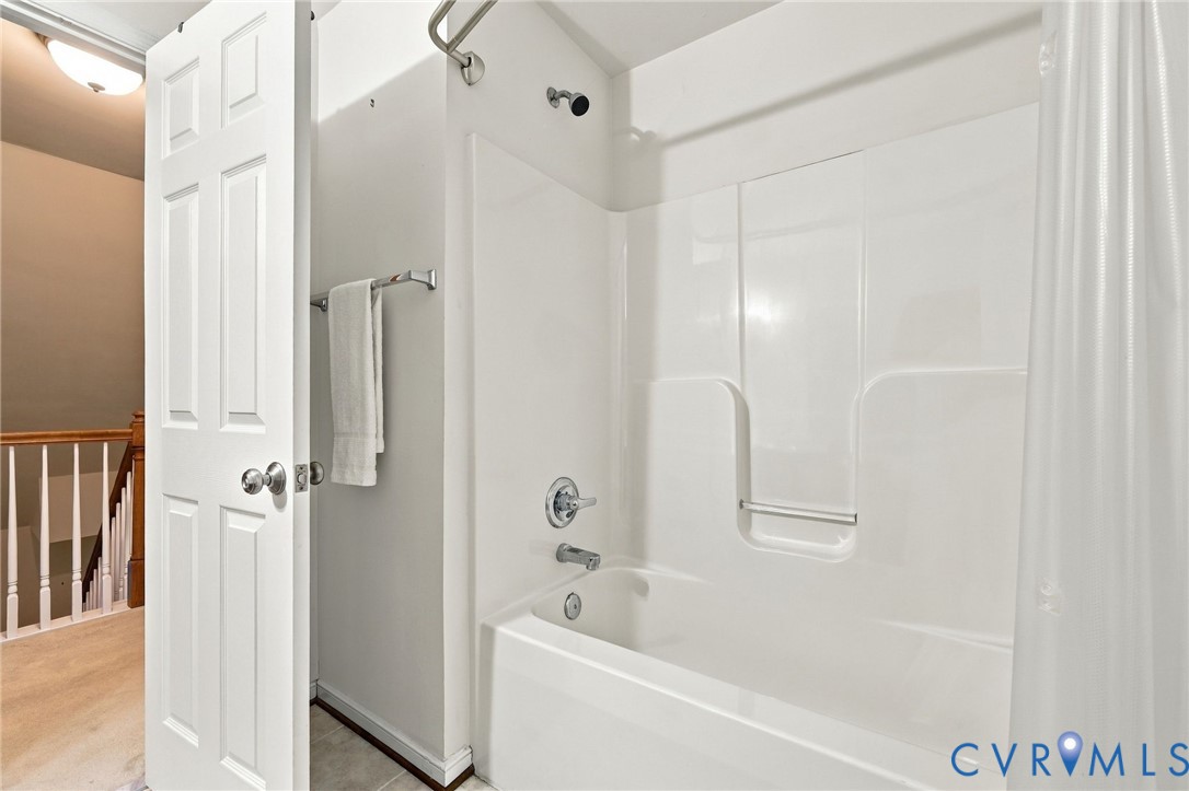White bathtub with an integrated shower, chrome fixtures, and a curved shower rod