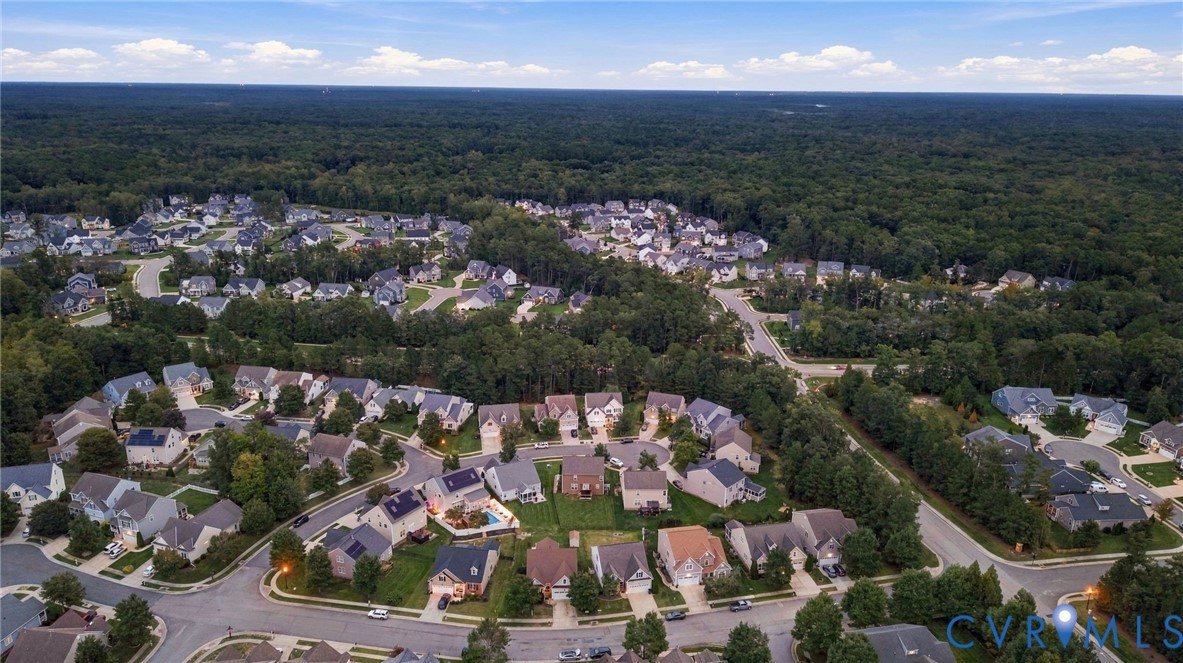 Aerial perspective showcasing a residential community bordered by extensive wooded areas, featuring numerous detached properties and established street infrastructure