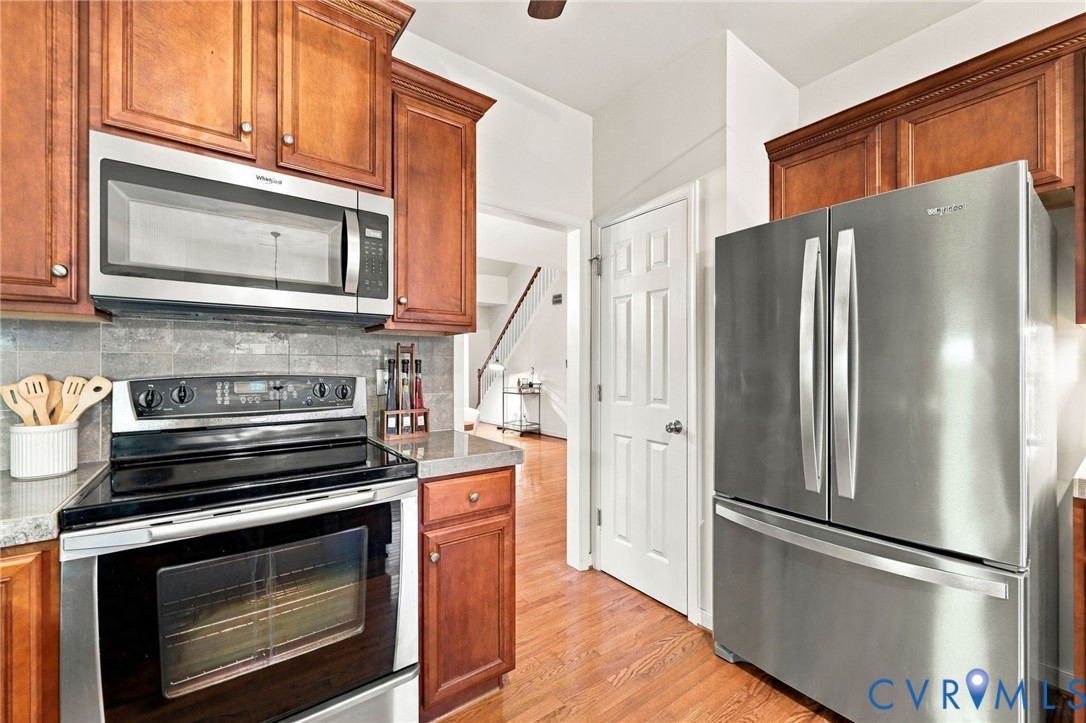 Kitchen featuring wood-finish cabinetry, stainless steel appliances, stone-look countertops, and a tile backsplash