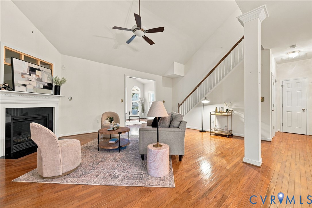 Vaulted ceiling with a ceiling fan, fireplace with a white mantel, wood-finish flooring, and a staircase with white balusters