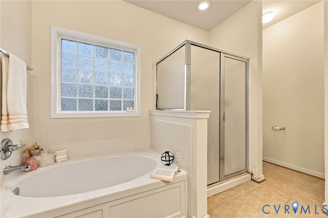 Soaking tub with a tiled surround, privacy glass window, and an enclosed shower with frosted panels and a metal frame