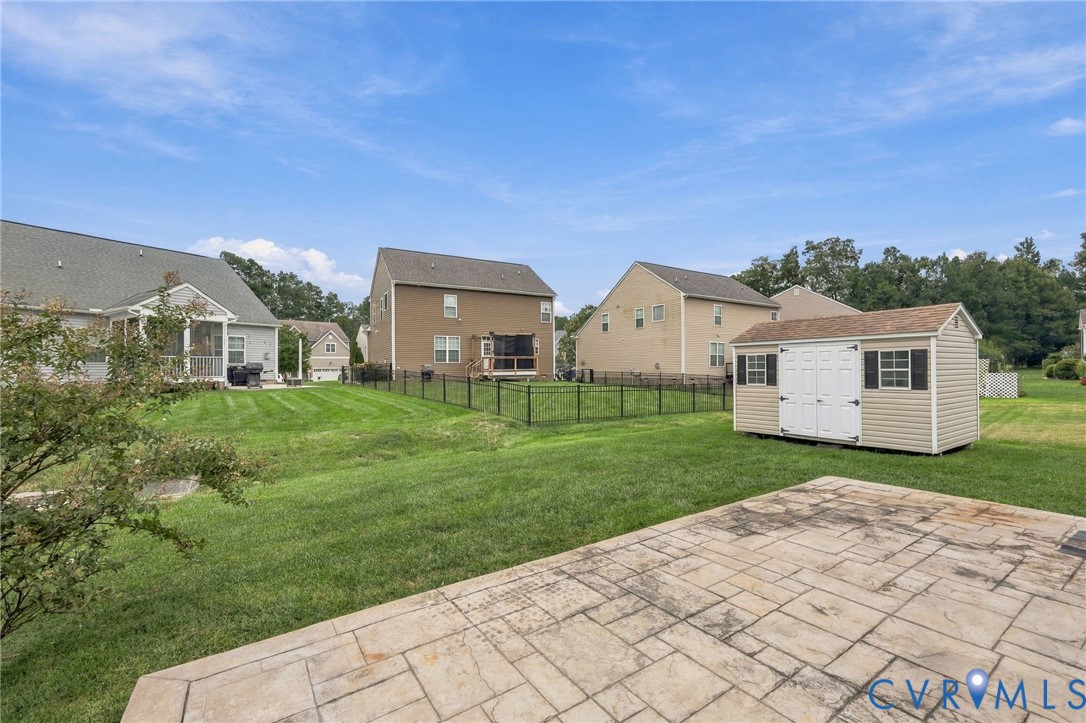 Spacious backyard featuring a stamped concrete patio, expansive lawn, and a detached storage shed