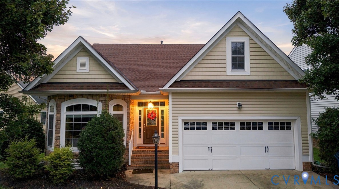 Charming brick and siding exterior featuring a covered front porch with arched entryway, dual gabled roofline, and a two-car garage with paneled doors