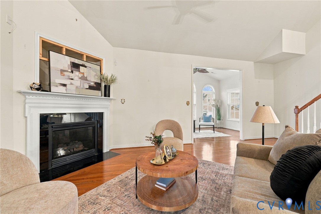 Vaulted ceiling, hardwood flooring, fireplace with a white mantel, and an open entryway